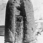 An ancient wooden artifact with a curved top and a rough surface, possibly an invention or tool.